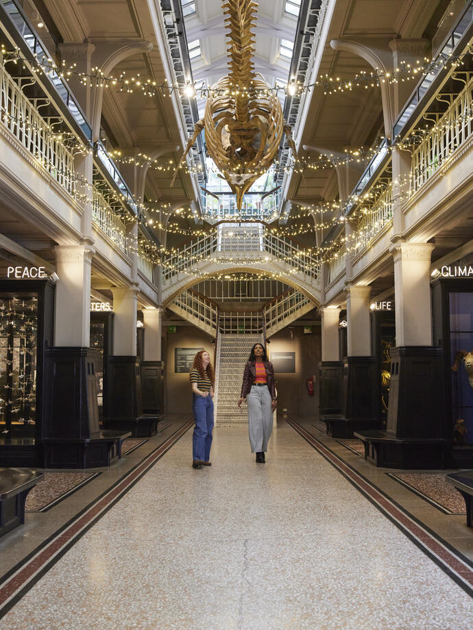 Two women talking, laughing visiting the prehistoric exhibition inside a large museum.