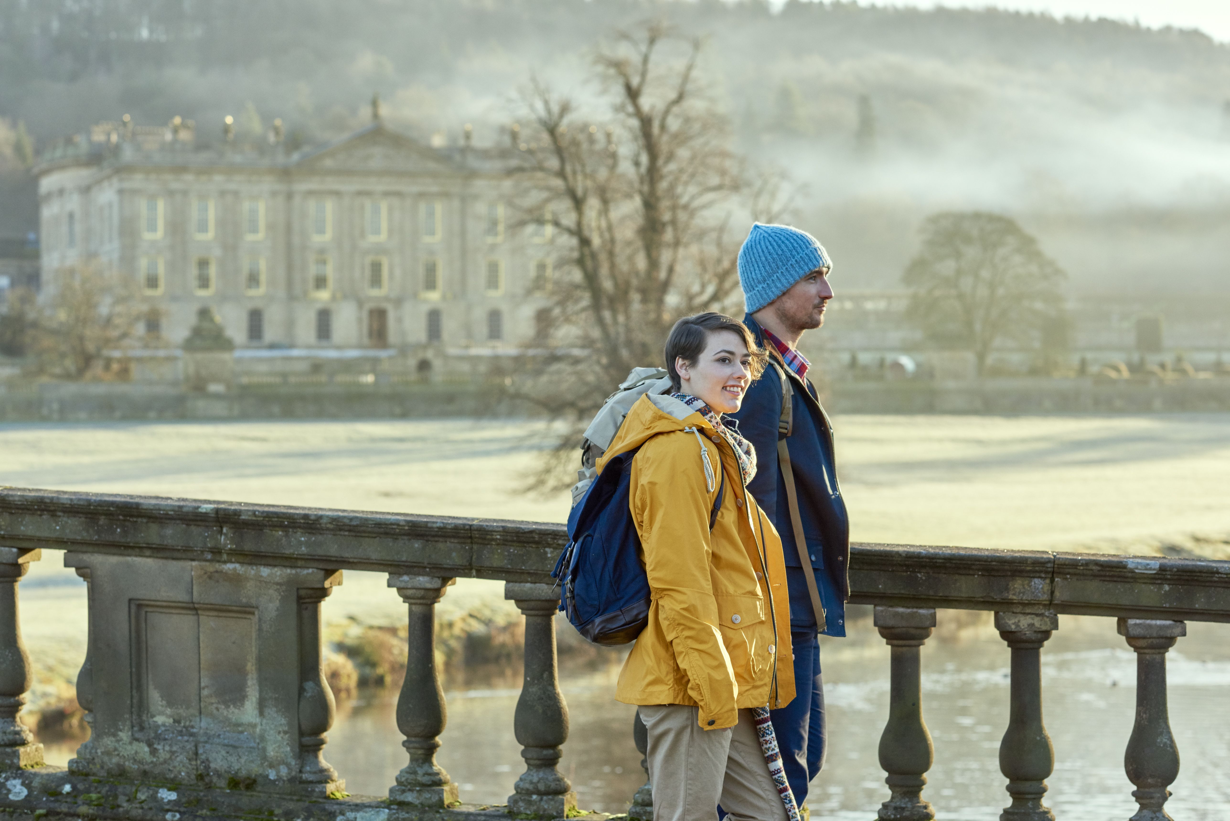 Couple walking on a stone bridge, a large country house in the backround