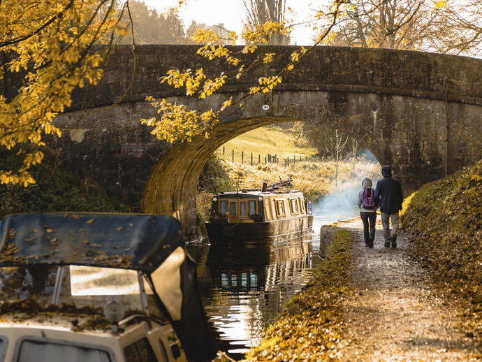 Man and woman walking beside a canal near a low bridge