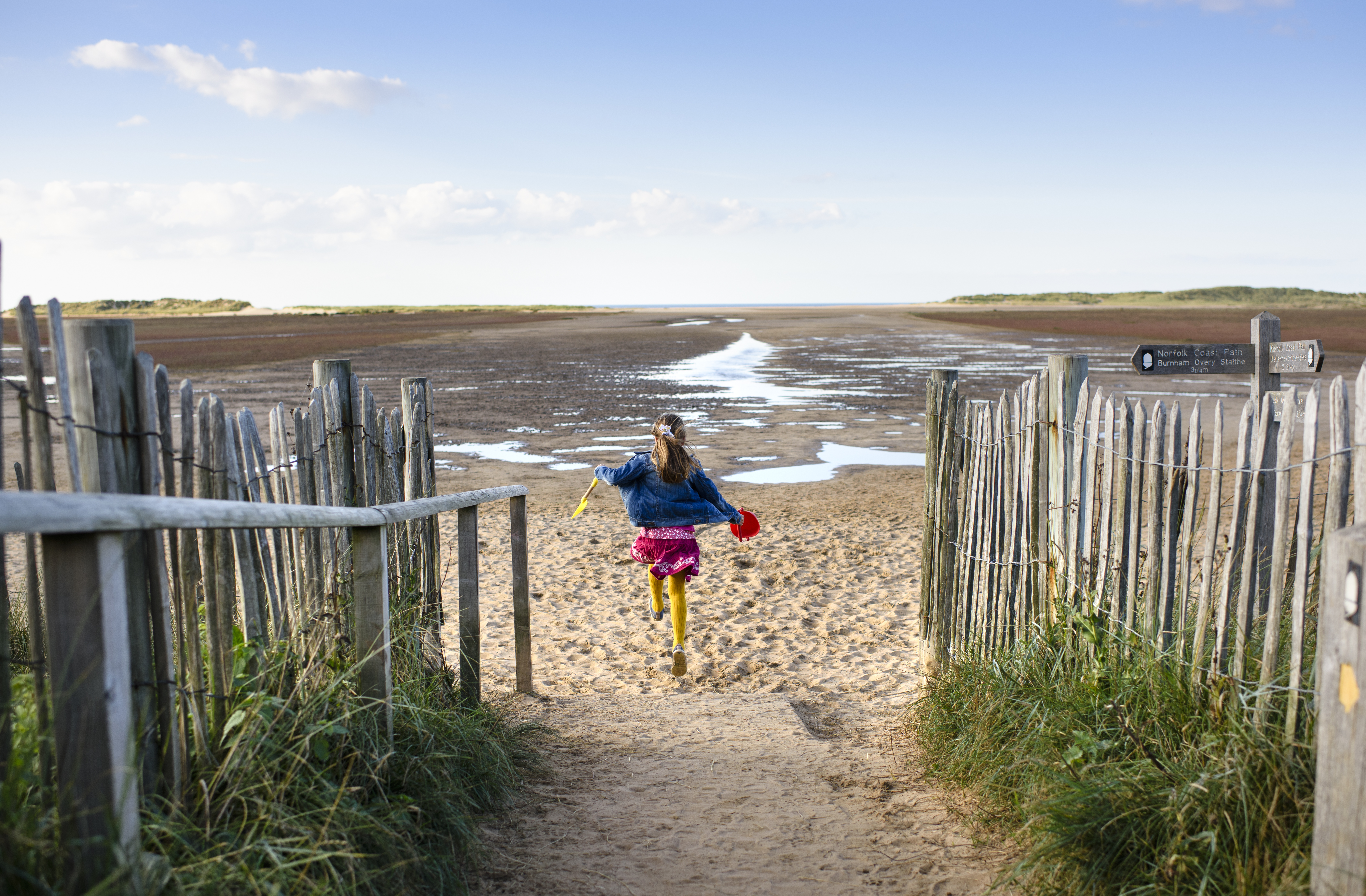 A girl running down a path to Holkham Beach