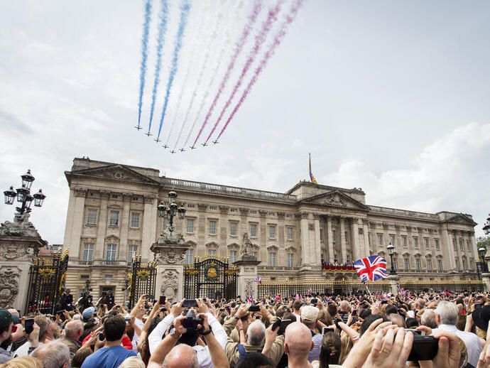 Jets with coloured smoke trailing behind fly in formation over crowds and a palace