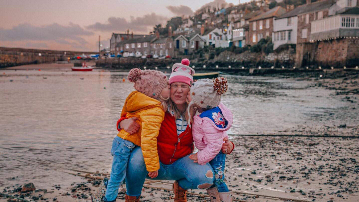Two children giving a woman a kiss on the cheek on a beach