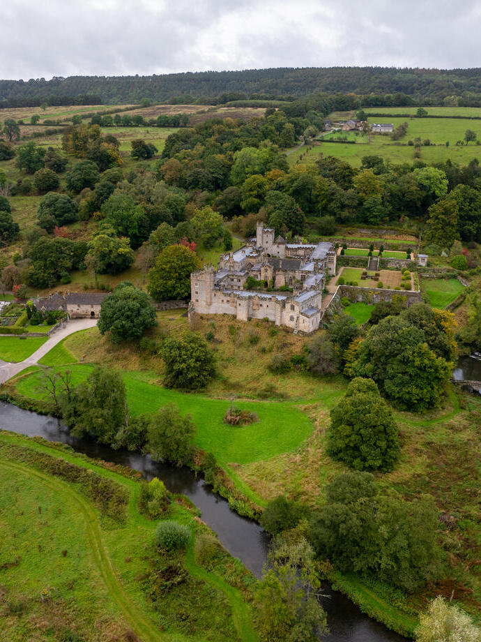 Aerial view of large manor house surrounded by green fields, trees, and a river in the countryside