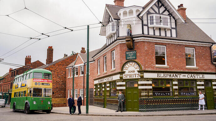 Historic street scene with a vintage green double-decker bus, brick buildings, and a corner pub named Elephant and Castle.