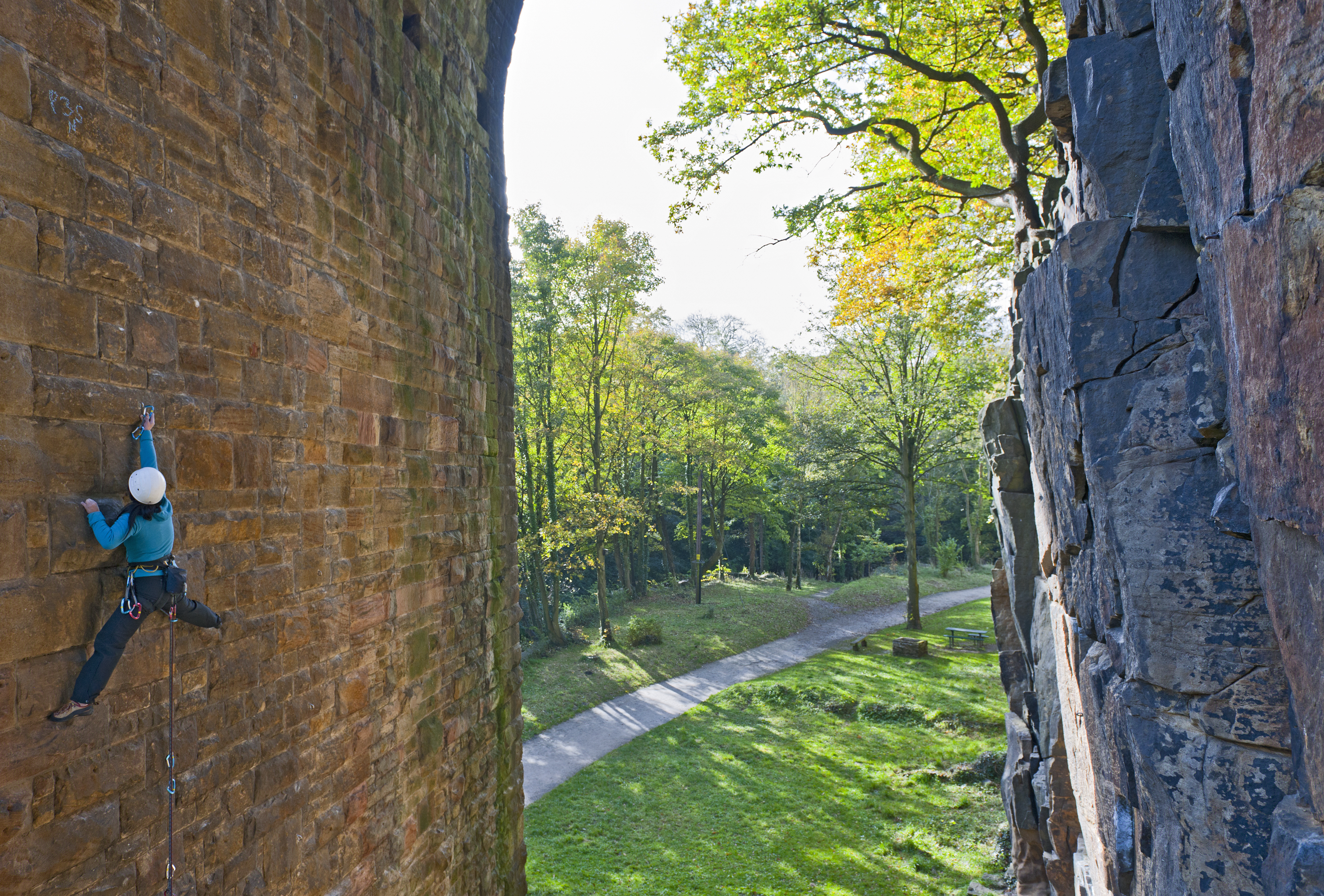 A climber using climbing gear scaling the underside of the arch of a bridge