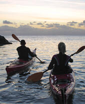 A couple kayaking off the coast of a rocky coastline.