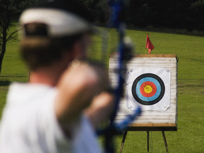A person aiming a bow and arrow at a target from distance.