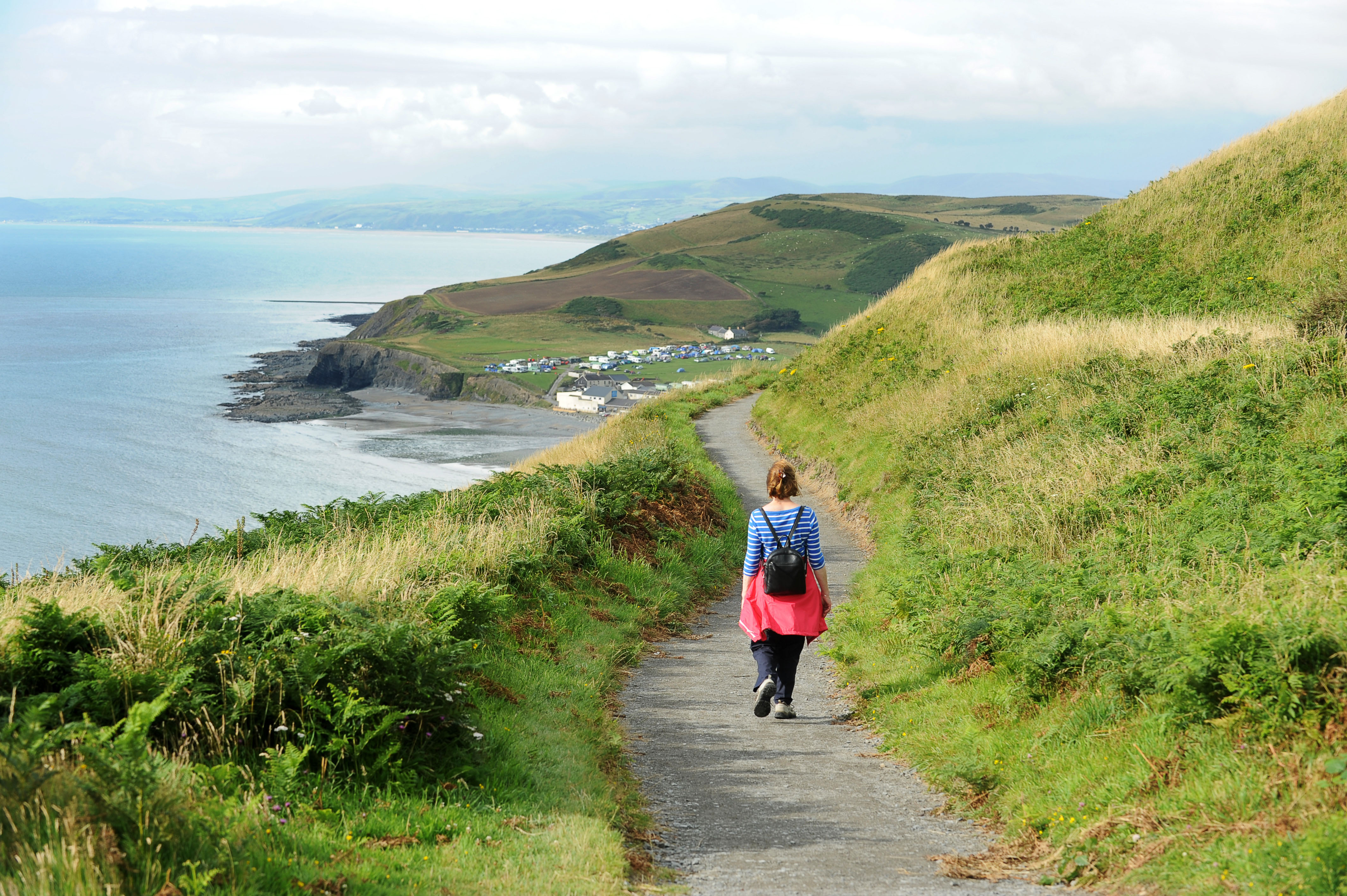 A woman strolling along a coastal path heading towards a seaside village.
