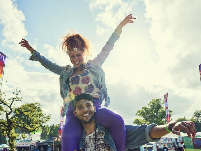 A woman sits on a man's shoulders at a festival in the summertime
