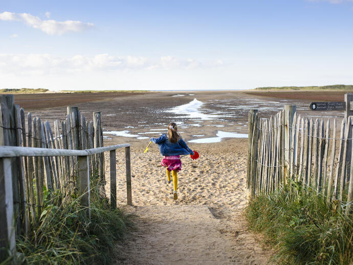 Una niña corriendo por un sendero hacia la playa de Holkham