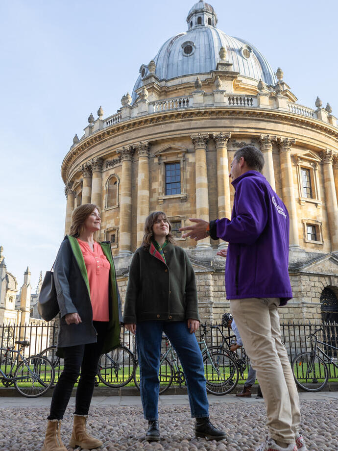 Two women listening to a tour guide outside an old dome shaped building.