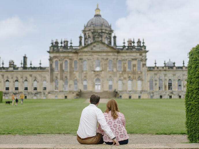 A man and a woman sit on a step looking towards a heritage building