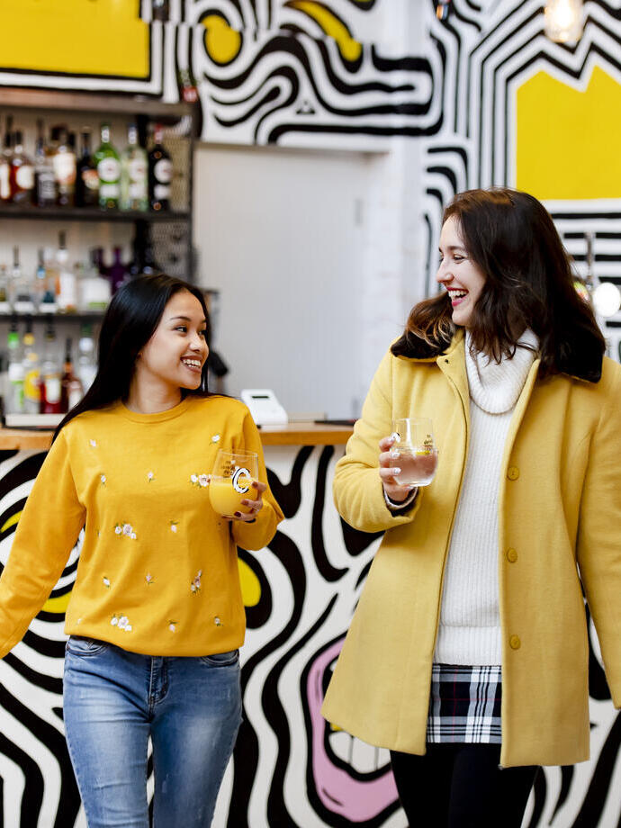 Two woman holding drinks and walking away from a bar