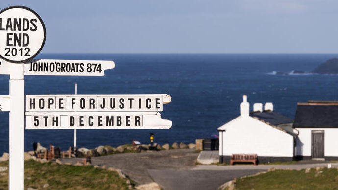 Witte wegwijzer op een klif met de zee en een wit gebouw in de verte