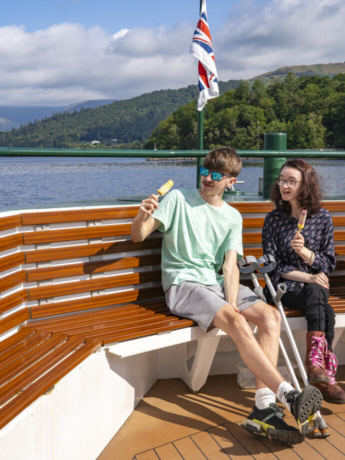 Three people sit at the end of a boat on a lake eating ice creams