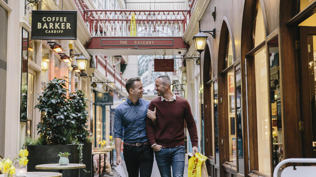 Ein männliches Paar, das Arm in Arm durch eine viktorianische Einkaufspassage spaziert