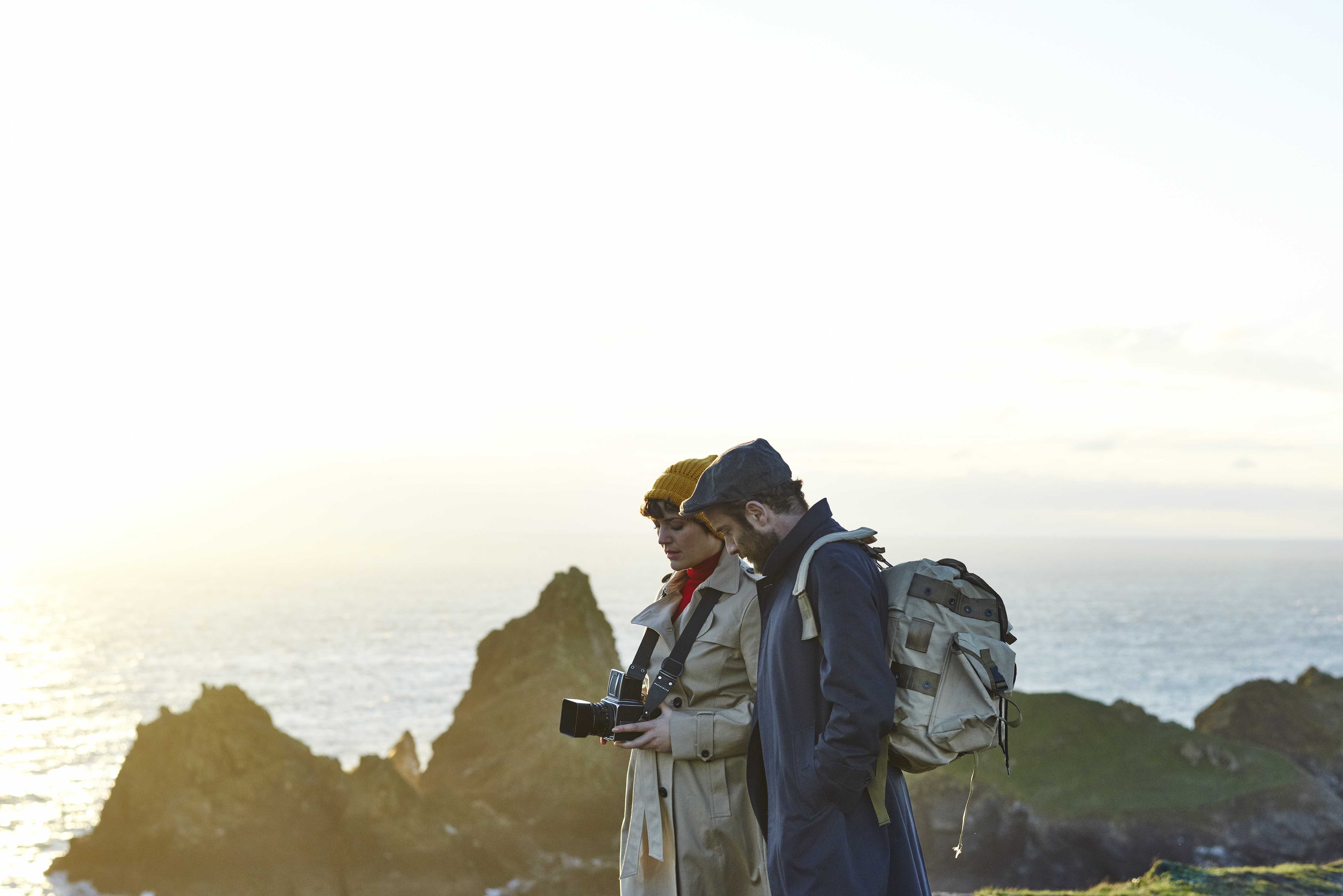 Couple standing on top of the cliffs, the woman holds a camera and the man wears a backpack