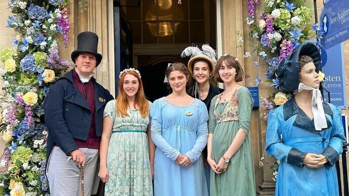 A group of people posing in period Victorian costume under a floral archway.