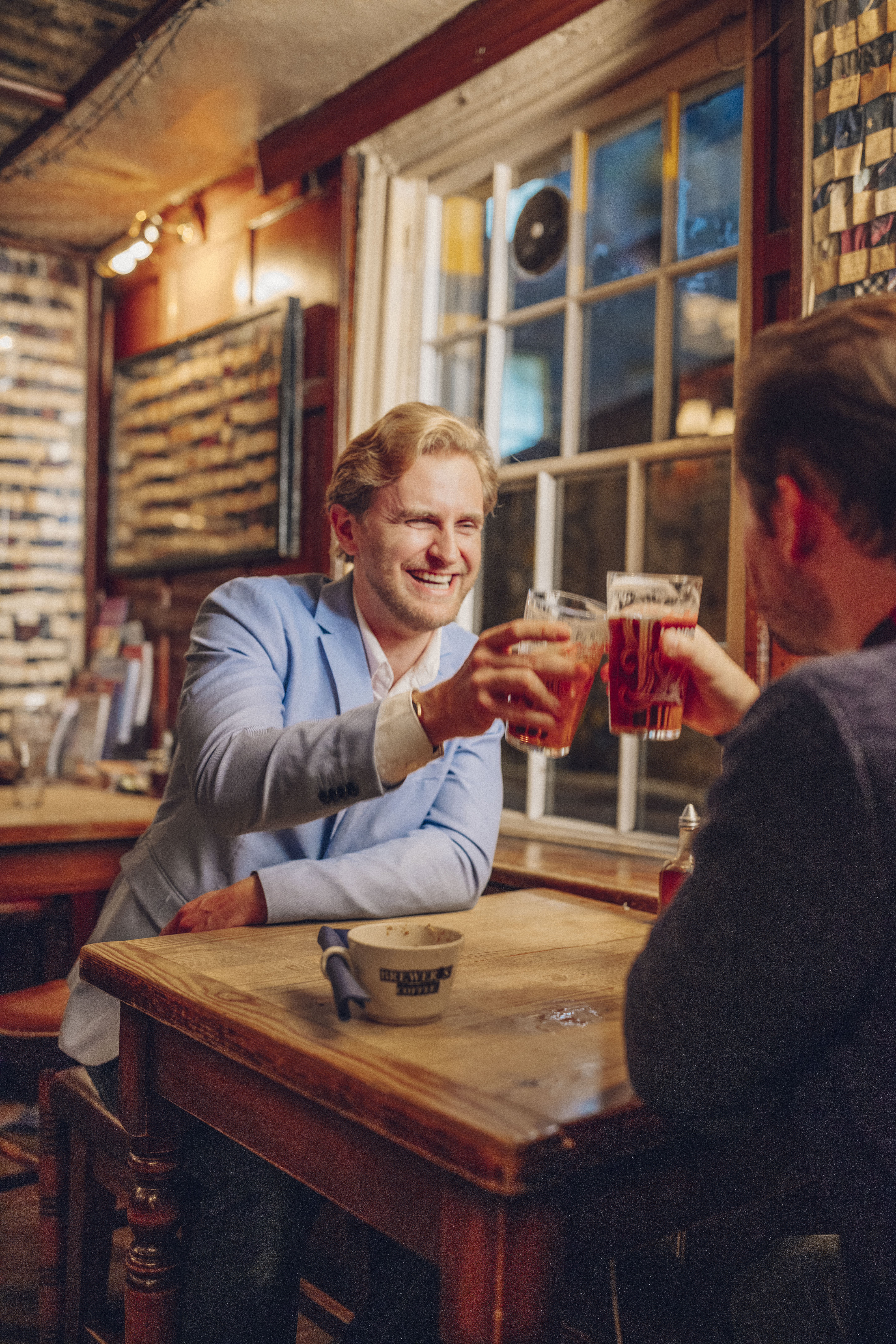 Two men sat in a pub toasting each other with pints of beer