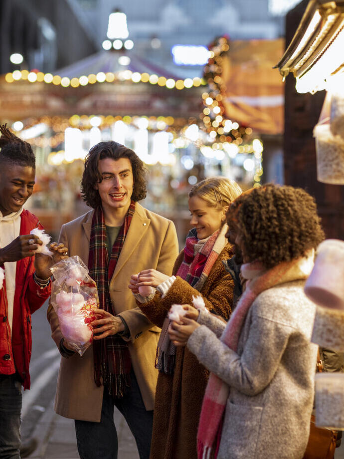 Groupe de jeunes amis partageant un sac de barbe à papa au marché de Noël.
