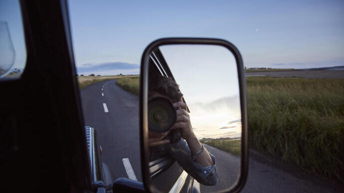 Reflexion eines Mannes mit einer Kamera im Seitenspiegel eines Autos