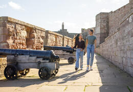 Two women walking along the walls of a castle past canons on display