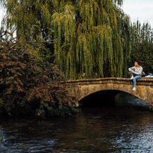 Woman sitting on a low stone bridge over a river in a village