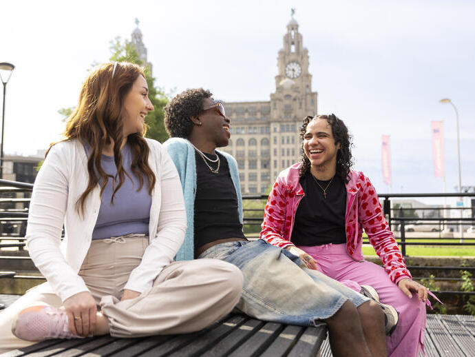 A group of friends sit together on a bench in front of an iconic building