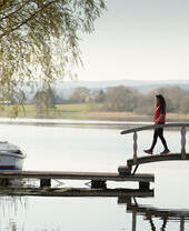 A woman stepping over a bridge, near a moored boat.