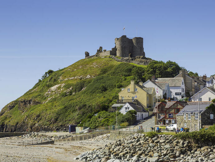 Un castello in cima a una collina accanto a una spiaggia, circondato da edifici colorati.