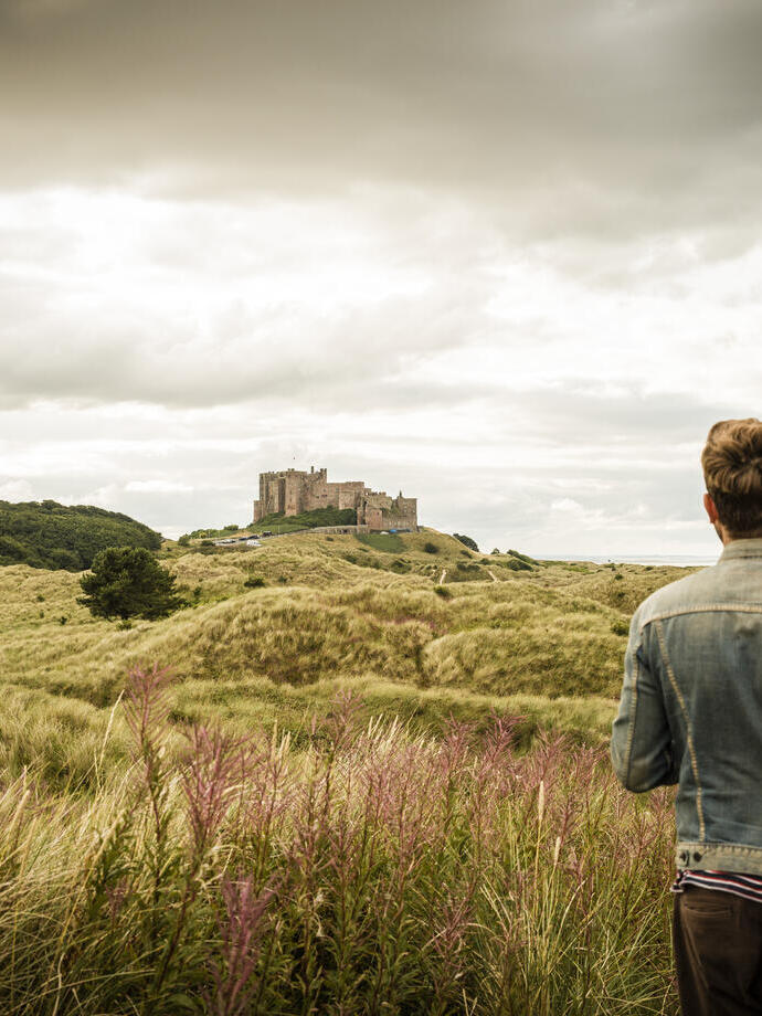 Hombre de pie entre las dunas mirando un castillo