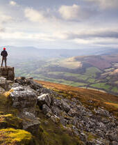 Mann auf einem weitläufigen, farbenfrohen Gebirge bei Sonnenuntergang mit Blick ins Tal