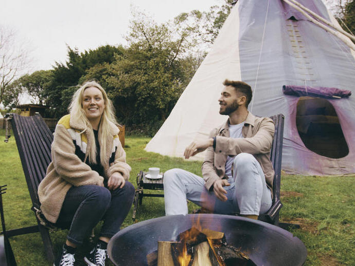 Man and woman sat around a fire, by a tepee