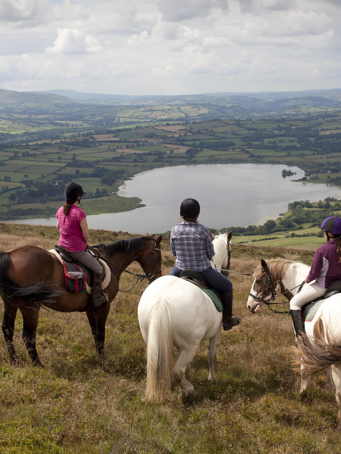 Un groupe de cavaliers sur une colline surplombant des terres agricoles et un lac.