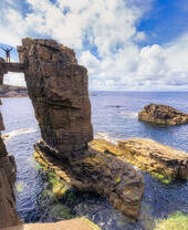 Man straddling two sea stacks overlooking a rocky outcrop and the ocean