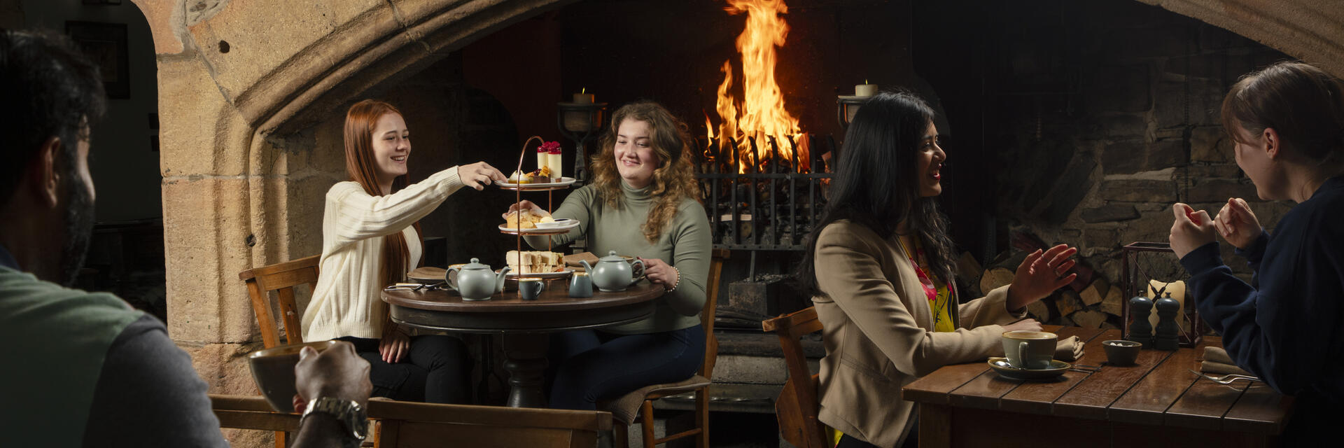 Two women enjoy an Afternoon Tea in front of a fire in an traditional historic pub
