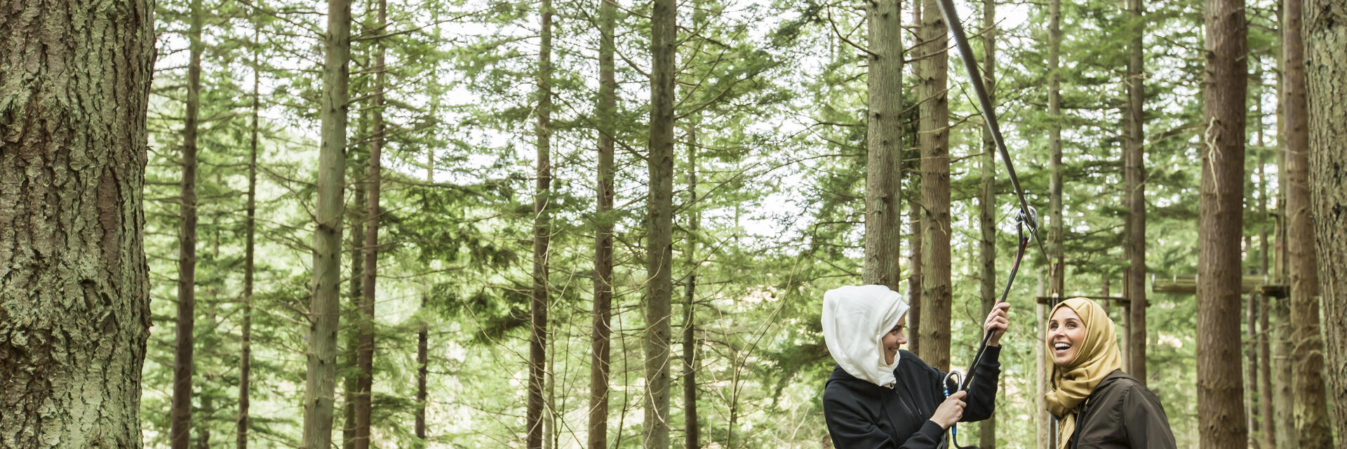 Two women preparing to go on a zipwire in the pine forest