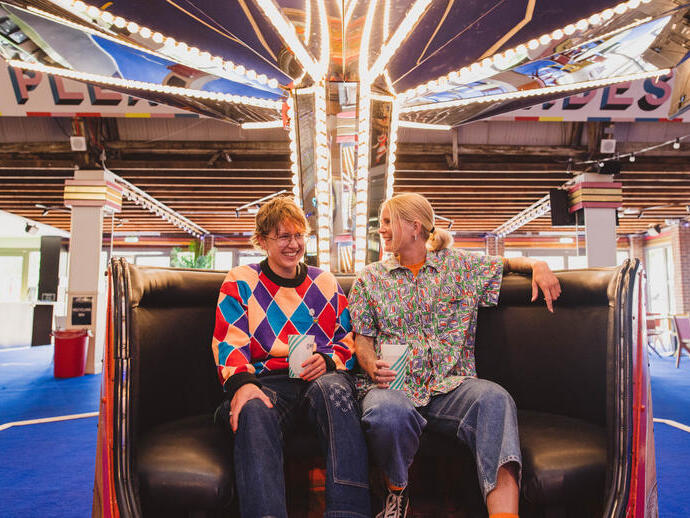 A man and a woman wearing roller skates sit in a retro teacup at a roller disco
