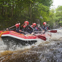 People wearing wetsuits and helmets paddling down a rapid