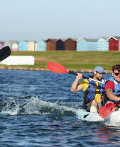 Friends kayaking on Mersea Island with beach huts in background
