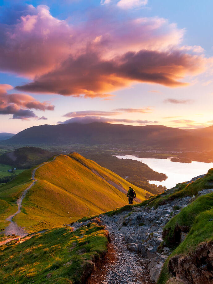 Hiker walking along a path on the mountain ridge at sunset