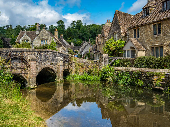 Blauer Himmel und Spiegelungen im malerischen Cotswold-Dorf Castle Combe.
