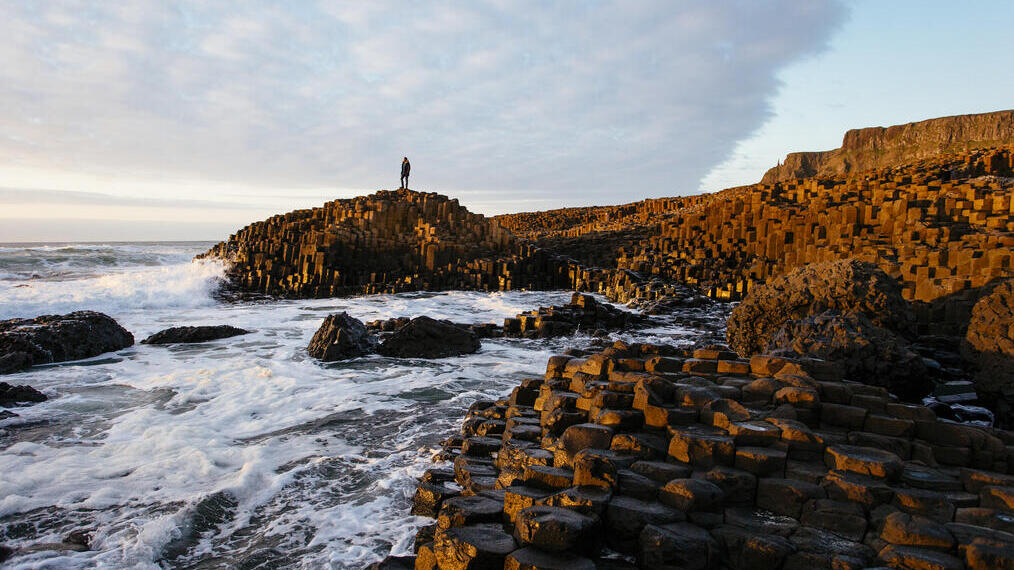 Man standing on a rock formation on the edge of the sea