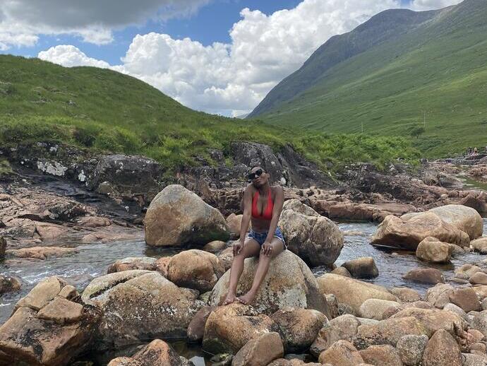 Woman sitting on a rock in a stream surrounded by mountains