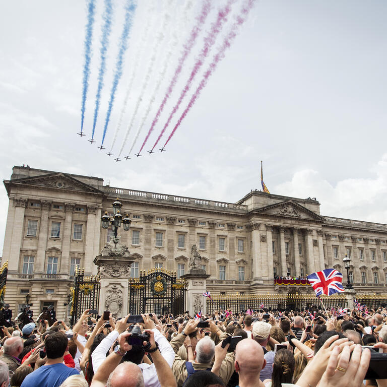 Jets with coloured smoke trailing behind fly in formation over crowds and a palace