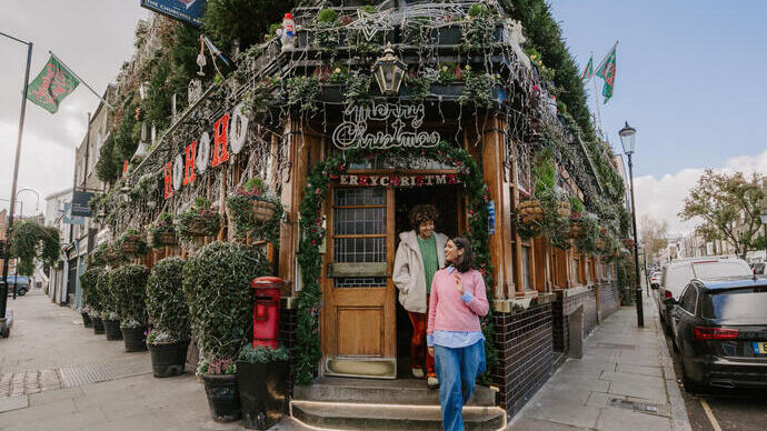 Two women leaving a pub covered with festive Christmas decorations.