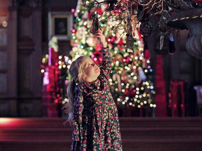 A girl looking at a hanging ornament in front of a decorated christmas tree at Bamburgh Castle's Christmas Kingdom