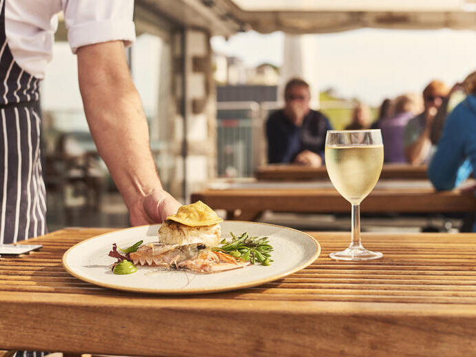 Ober die een bord met eten op tafel zet naast een glas wijn