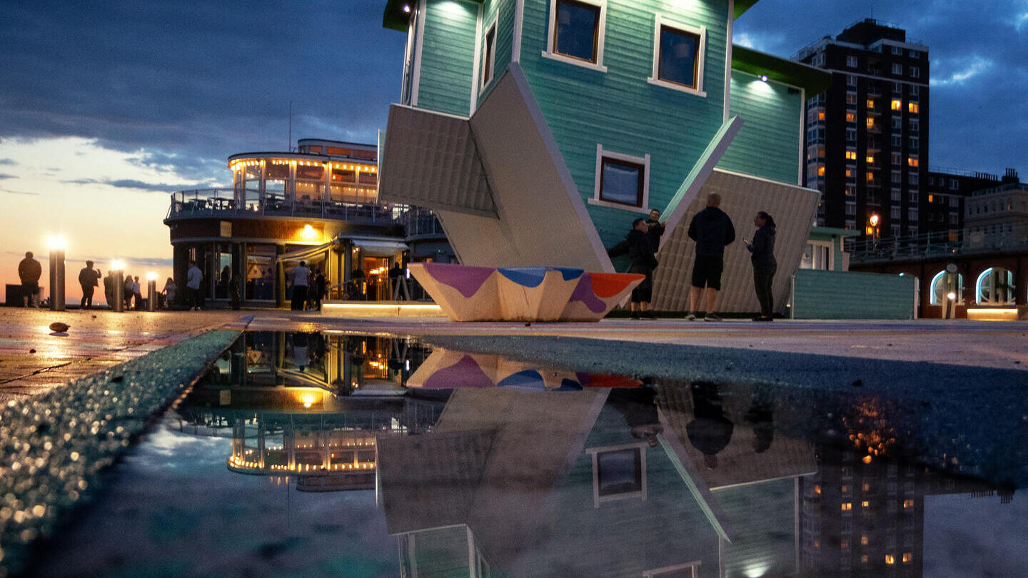 People outside a house that is upside down in the evening