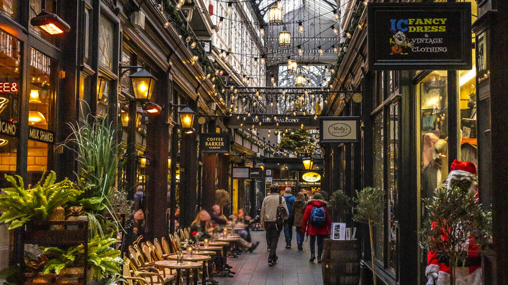 متسوقون يسيرون في ممر تسوق فيكتوري جميل توجد على جانبيه متاجر صغيرة ومطاعم